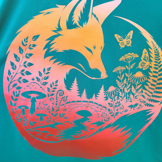 A close-up of a circular graphic print featuring a fox head and forest motifs in yellow and orange tones over a teal background.